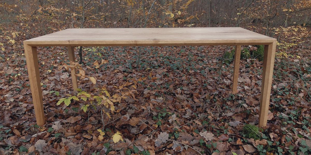 Schlichter Esstisch aus Massivholz mit schlanken Beinen im herbstlichen Wald auf Laub