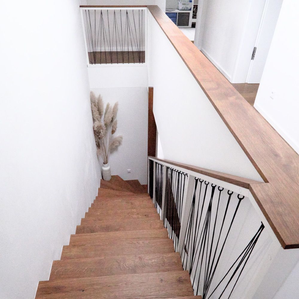 Massivholztreppe mit dunklem Eichenhandlauf und Schnurspannungs-Geländer, Blick von oben ins Treppenhaus