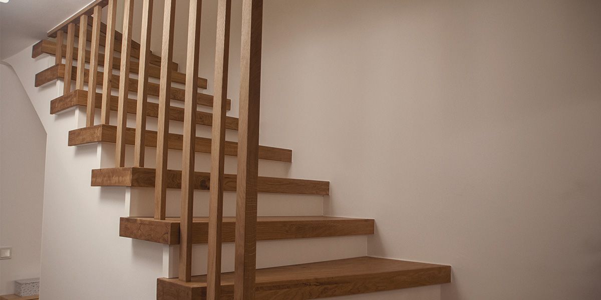 Massivholztreppe aus Eiche mit filigranem Stabgeländer und freischwebenden Stufen an weißer Wand