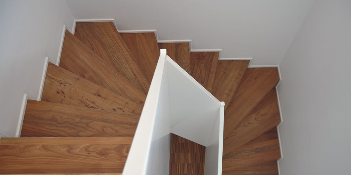 Gewendelte Vollholztreppe mit weißer Wange, Blick von oben auf die markante Holzmaserung der Stufen