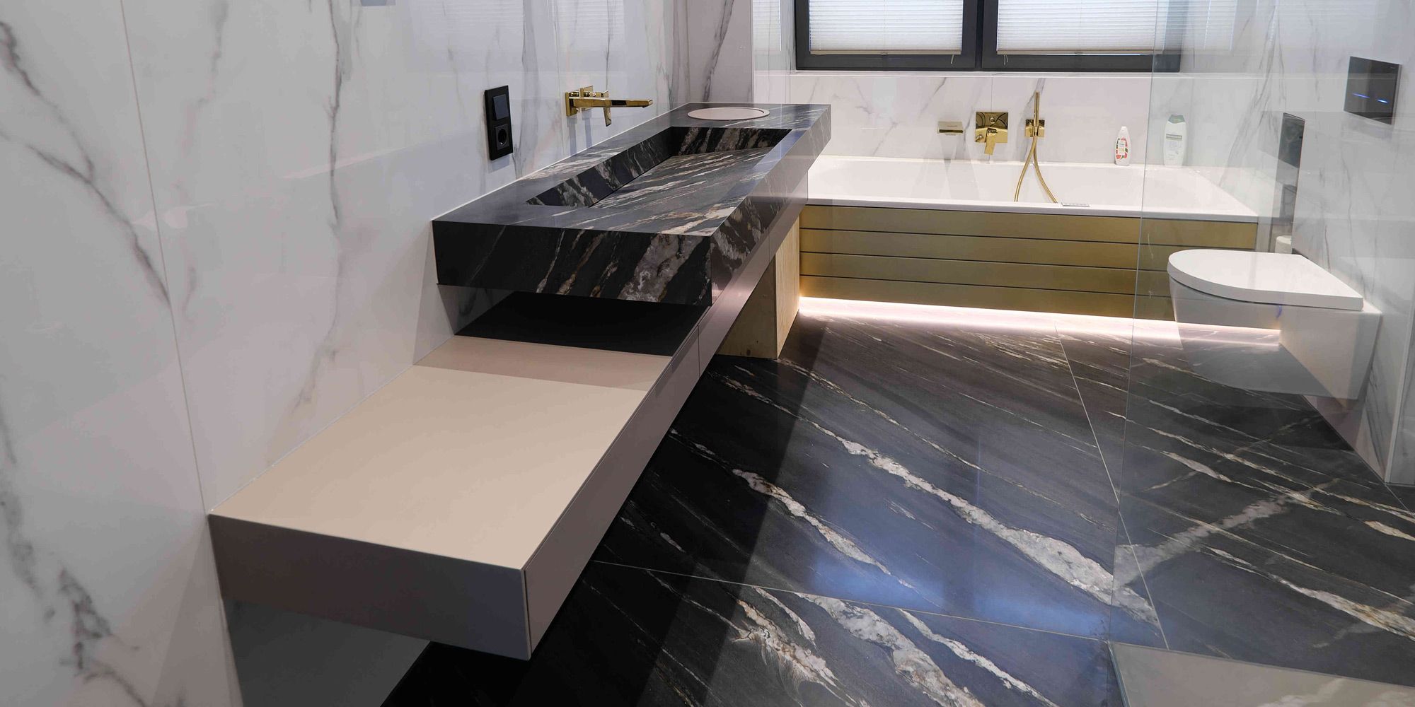 Luxusbad mit schwarzem Marmor-Waschtisch, Messing-Armaturen und goldener Badewannenverkleidung