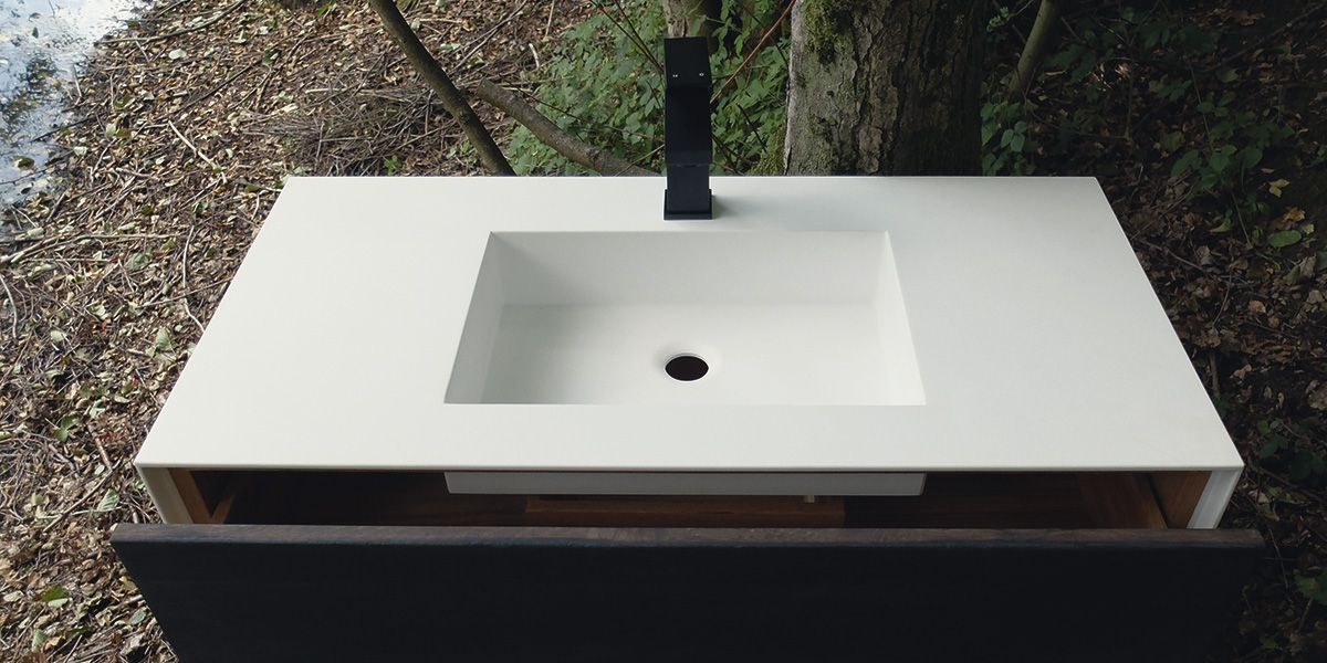Waschtisch mit hellem Mineralwerkstoff-Becken und schwarzer Standarmatur, im Wald am See fotografiert