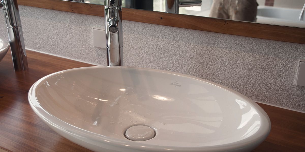 Ovales Keramik-Aufsatzwaschbecken auf Massivholzplatte mit Chromarmatur im Detail