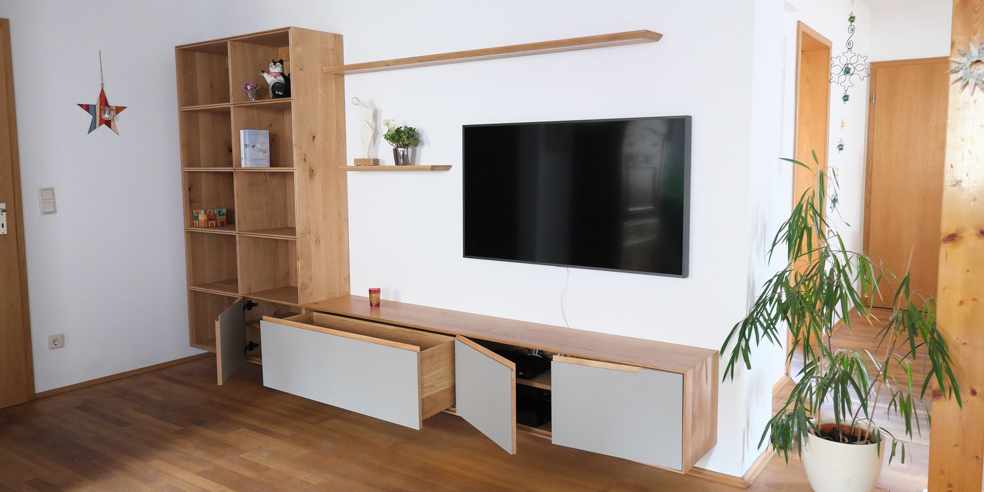 Eichen-Wohnwand mit offenem Regal und TV-Lowboard mit hellgrauen Klappen im Wohnzimmer