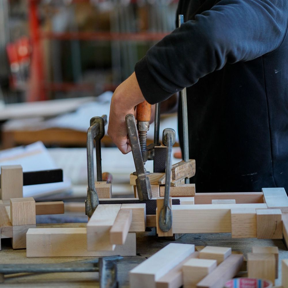 Schreiner spannt Holzverbindung mit Schraubzwinge auf der Werkbank in der Werkstatt ein