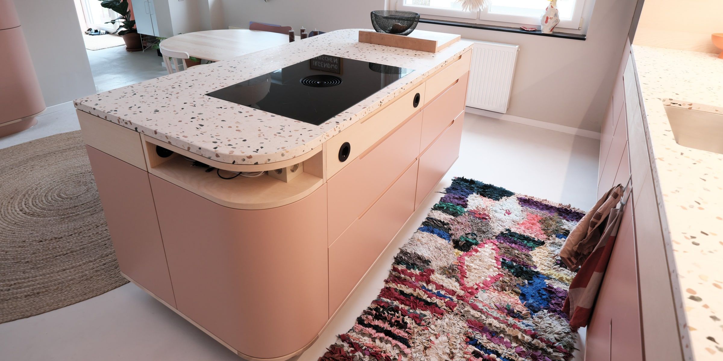 Rosa Kücheninsel mit Terrazzo-Arbeitsplatte, Kochfeld und buntem Berberteppich
