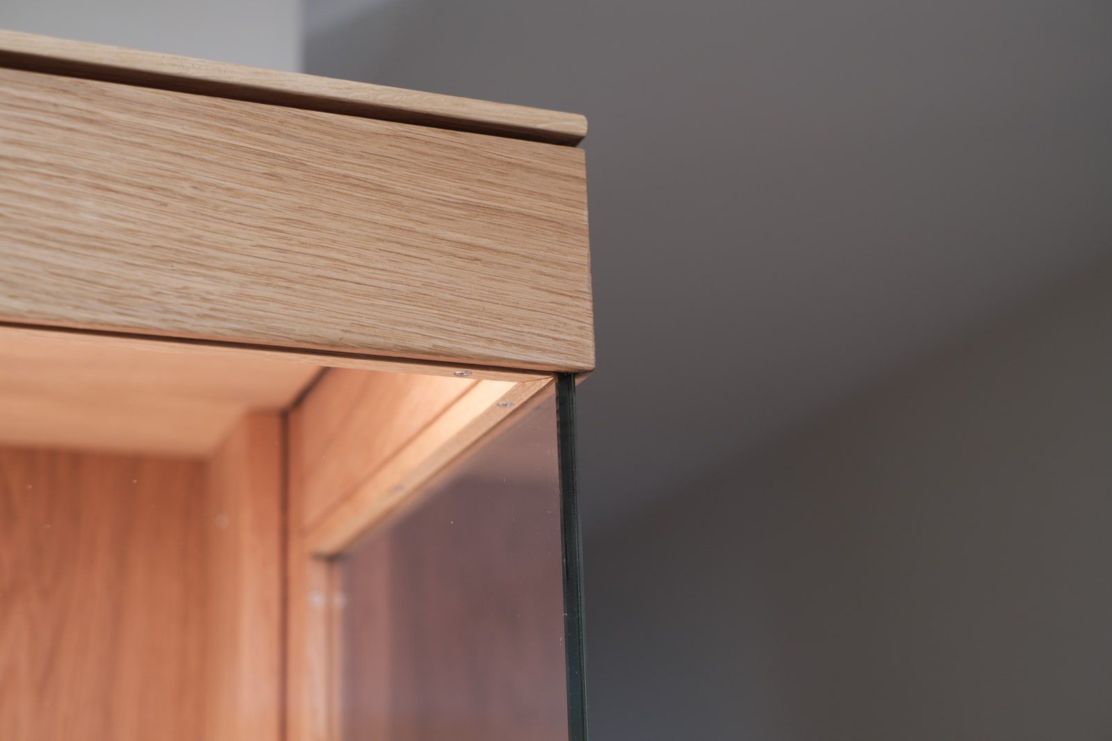 Detailaufnahme einer Eichenschrank-Ecke mit Glastür und warmer Innenbeleuchtung
