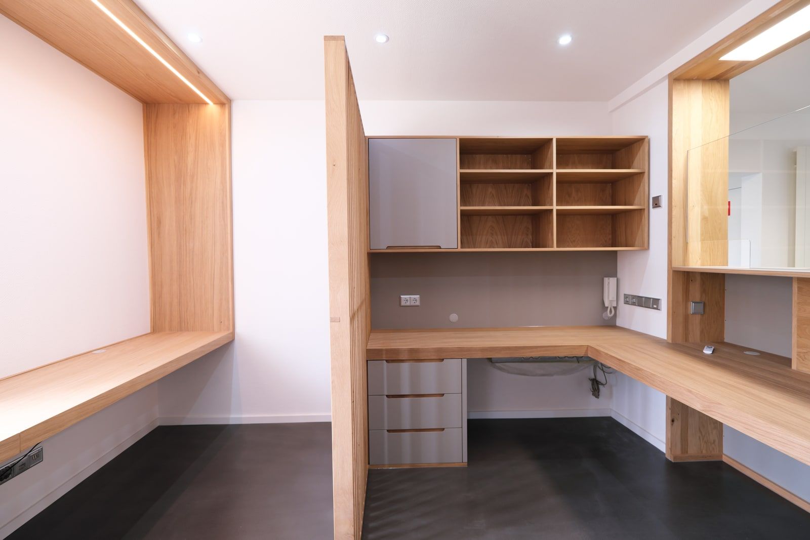 Büroeinbau mit Eichen-Eckschreibtisch, offenem Regal und indirekter Beleuchtung in der Praxis