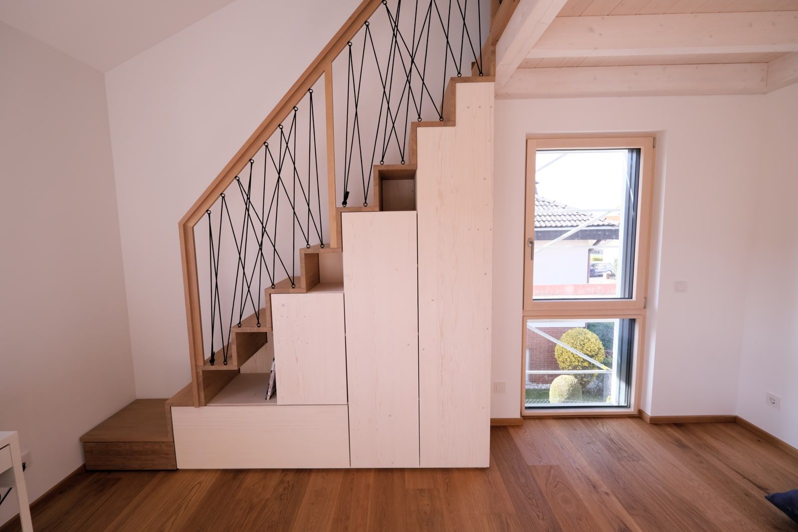 Maßgefertigte Massivholztreppe mit weißem Stauraum-Unterbau und Rautenseilgeländer