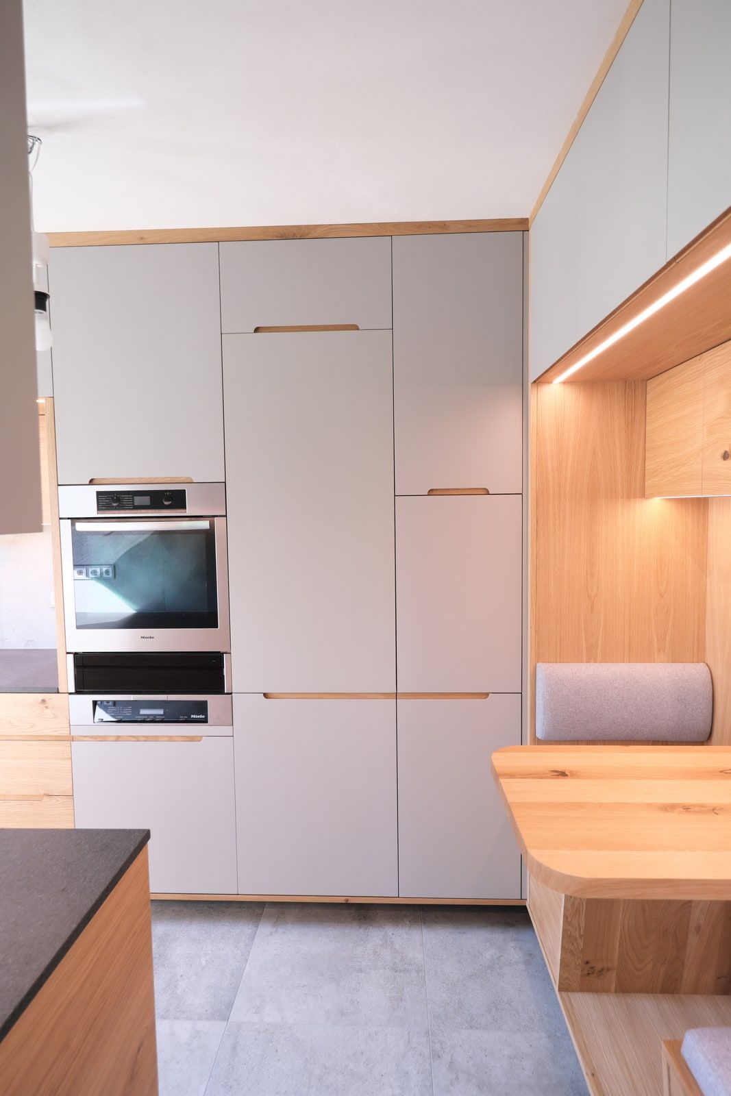 Moderne Küche mit grauem Hochschrank, Miele-Einbaubackofen und Eichenholz-Sitznische