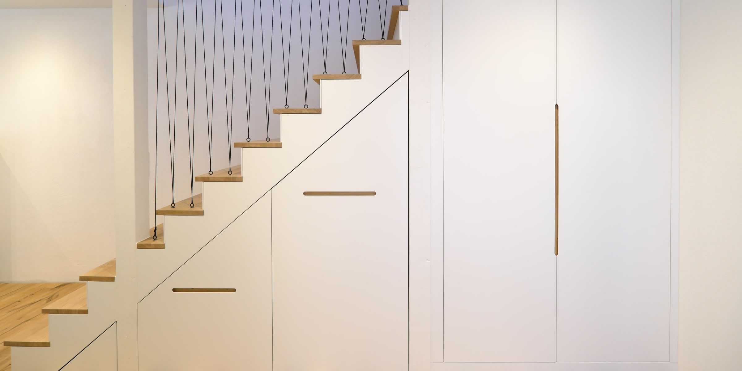 Design-Treppe mit integriertem Stauraumschrank, weißen Fronten und Eichenholz-Griffleiste