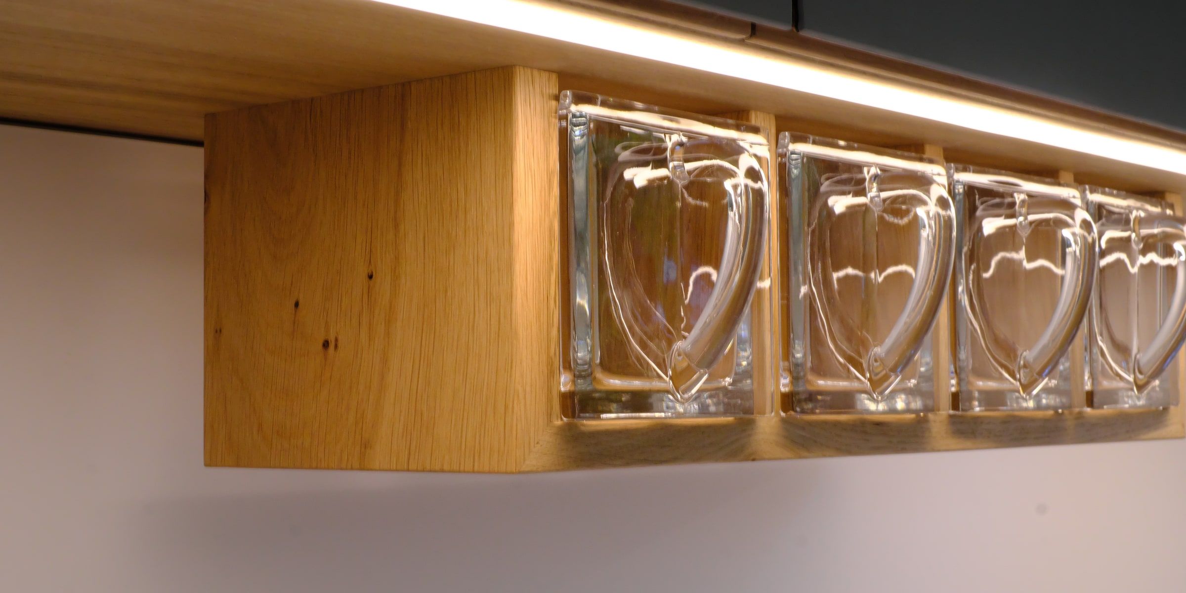 Glastassen hängen an Massivholzregal mit LED-Unterbauleuchte in der Küche