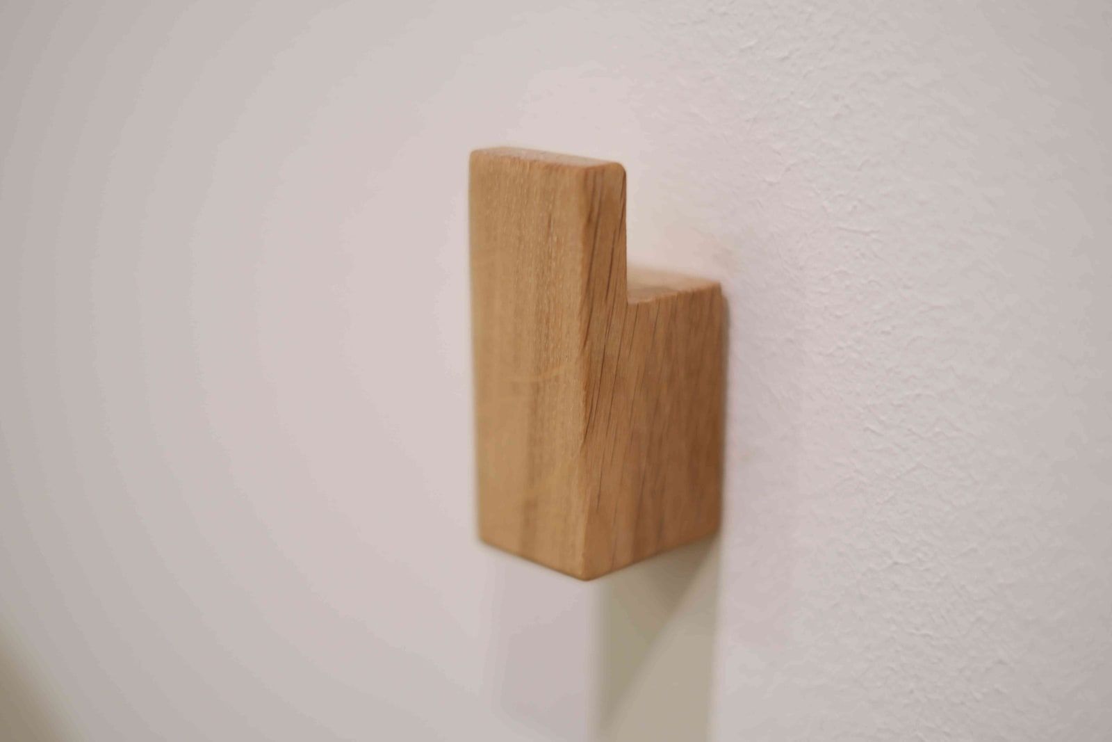 Massiver Garderobenhaken aus Eichenholz in schlichter L-Form an weißer Wand