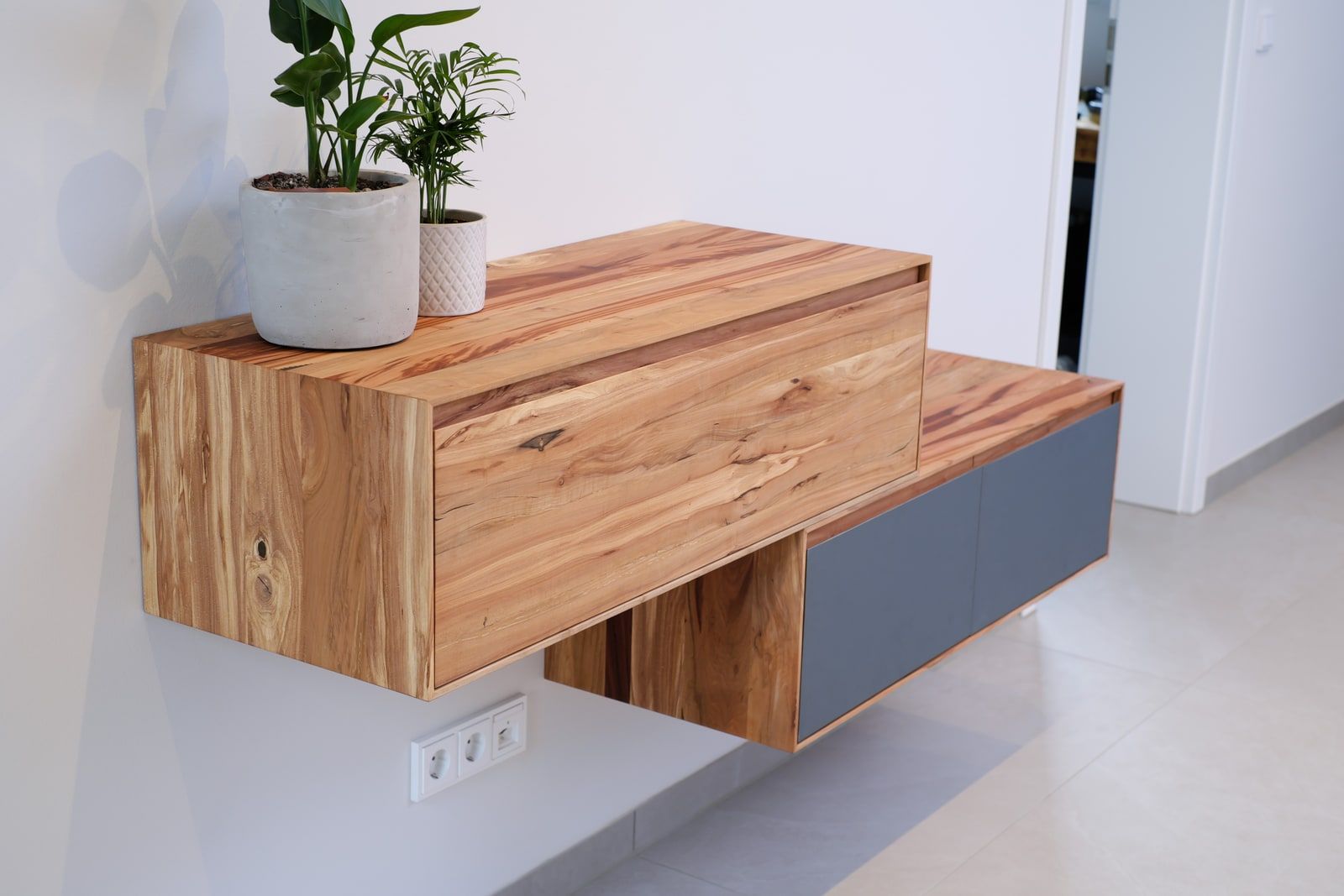 Schwebendes Sideboard aus Massivholz mit grauen Klapptüren über hellem Fliesenboden