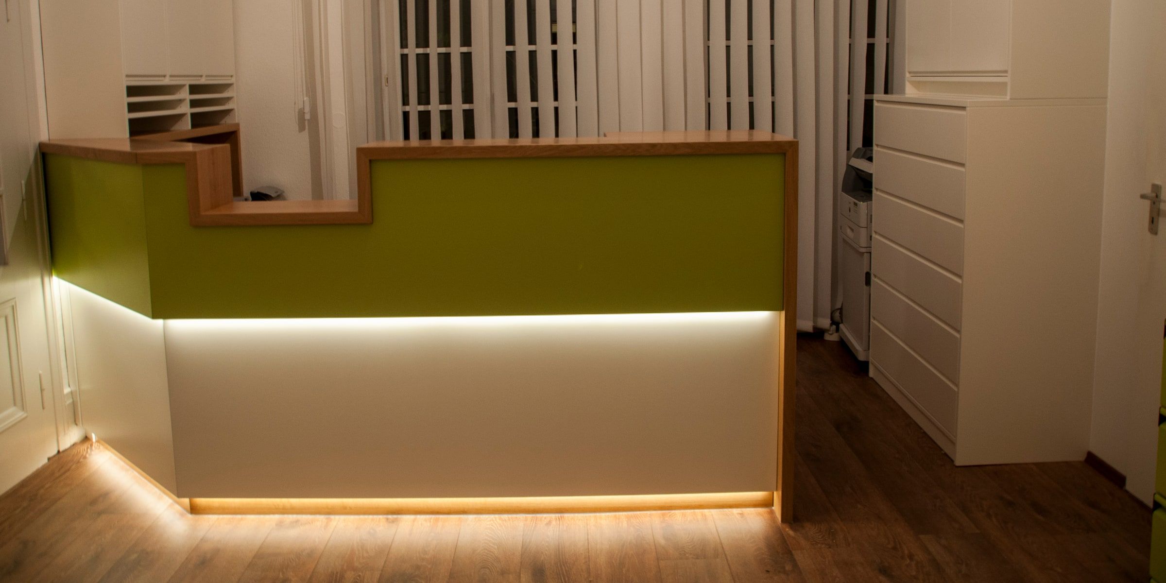 Maßgefertigter Empfangstresen in Grün-Weiß mit warmer LED-Unterbeleuchtung