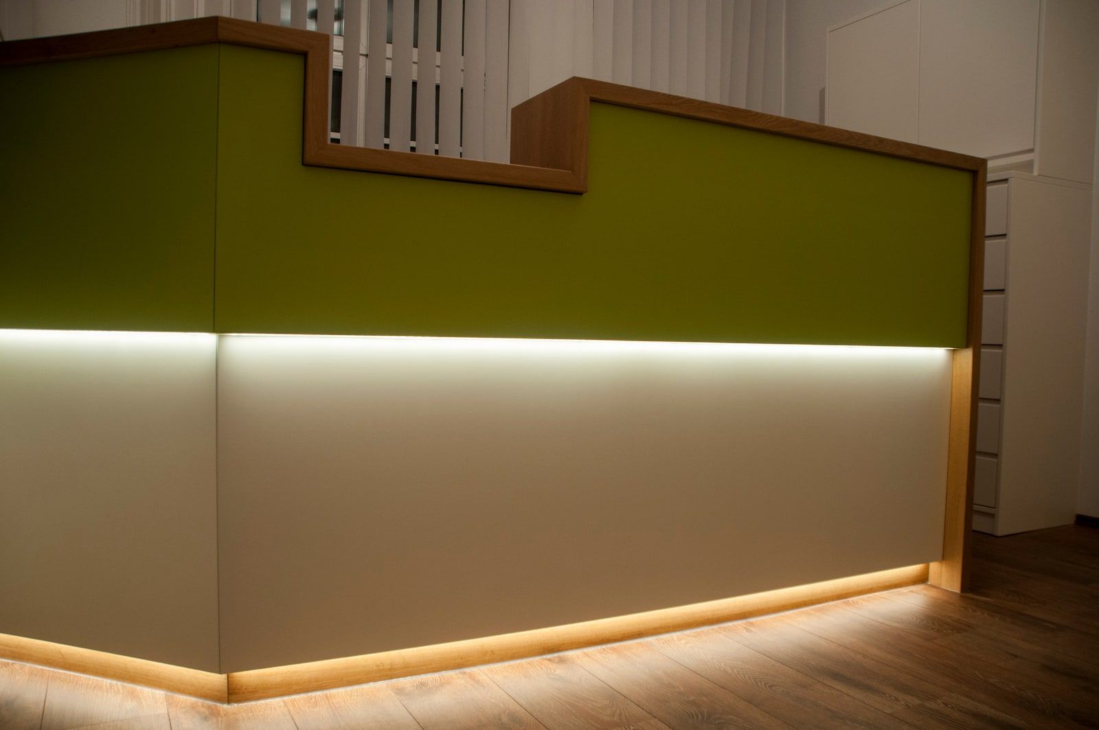 Empfangstresen mit gestufter grüner Front, Holzkante und warmer LED-Unterbeleuchtung
