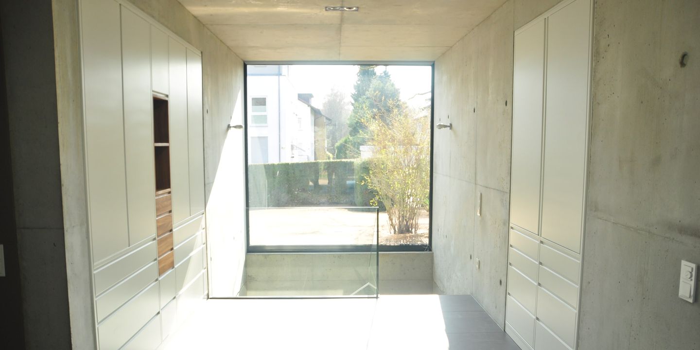 Raumhohe weiße Einbauschränke im Flur mit Sichtbetonwänden und Glasfront zum Garten