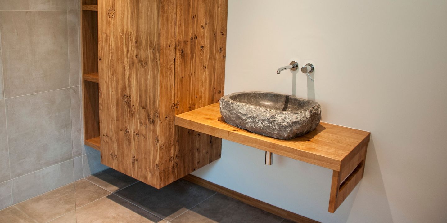Astreicher Eichen-Hochschrank neben Waschtisch mit Naturstein-Aufsatzbecken
