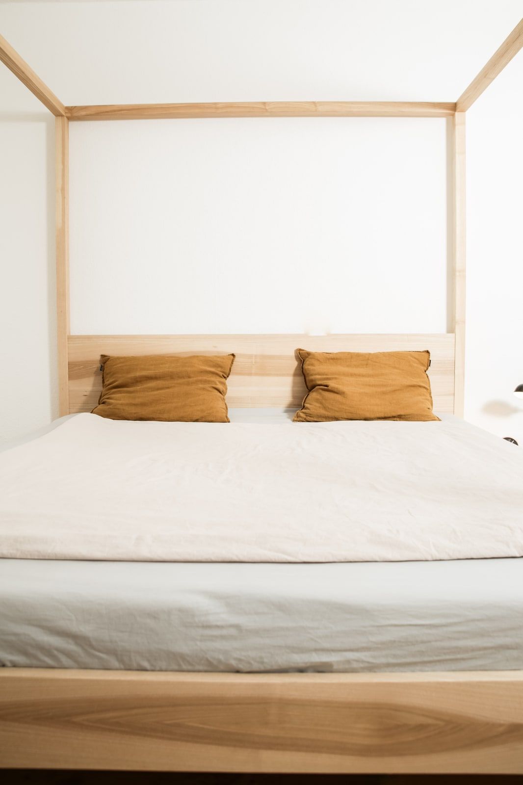 Helles Himmelbett aus Massivholz mit weißer Bettwäsche und Senfkissen